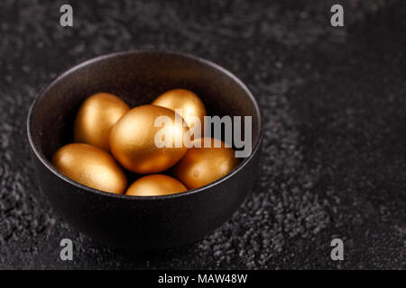 Eggs, painted in gold for the holiday. Golden eggs in a black cup on a black textured background. Easter eggs. Stock Photo