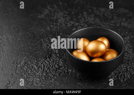 Eggs, painted in gold for the holiday. Golden eggs in a black cup on a black textured background. Easter eggs. Stock Photo