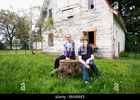 Two children sitting in front of a barn. Stock Photo