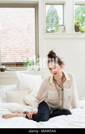Portrait of a woman sitting on her bed wearing a lot of necklaces. Stock Photo