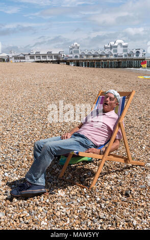 Elderly man wearing a knotted handkerchief on his head relaxing on the beach. Southsea, England UK Stock Photo