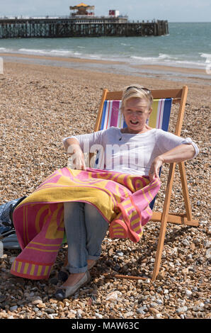 Woman sitting in a deckchair on the beach on a windy day. Southsea, England UK Stock Photo