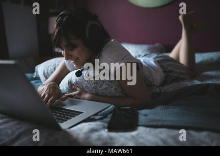 Woman using laptop with headset in bedroom Stock Photo