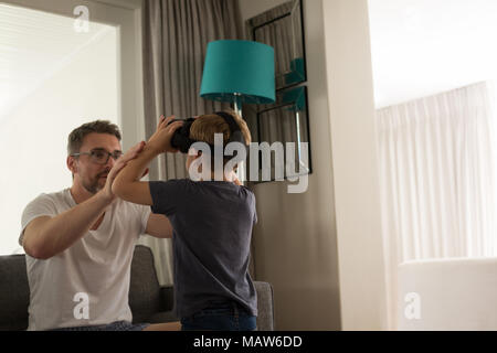Father helping his son in using virtual reality headset in living room Stock Photo