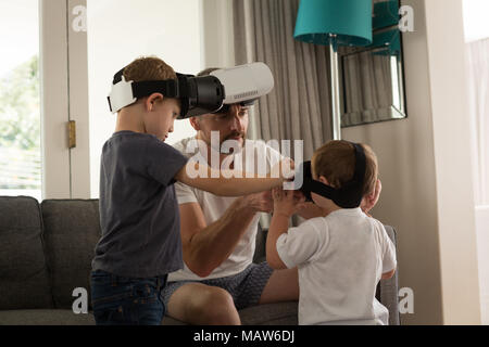 Father helping his son in using virtual reality headset in living room Stock Photo