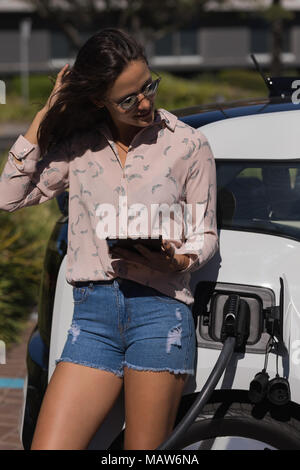 Woman using digital tablet while charging electric car Stock Photo