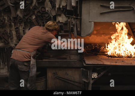 Blacksmith heating metal rod in fire Stock Photo