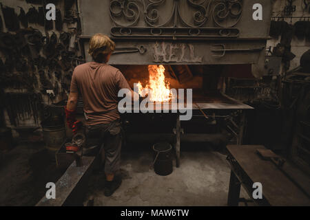 Blacksmith heating metal rod in fire Stock Photo