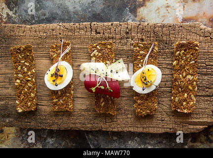 Row of raw bread with sunflower seeds, carrots, sesame, flax seed and other vegetables. Egg halves, microgreen, cucumber and beetroot slices on old wo Stock Photo