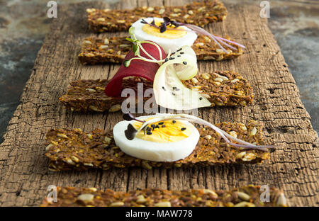 Row of raw bread with sunflower seeds, carrots, sesame, flax seed and other vegetables. Egg halves, microgreen, cucumber and beetroot slices on old wo Stock Photo