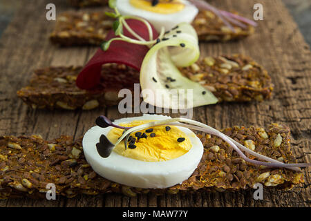 Row of raw bread with sunflower seeds, carrots, sesame, flax seed and other vegetables. Egg halves, microgreen, cucumber and beetroot slices on old wo Stock Photo