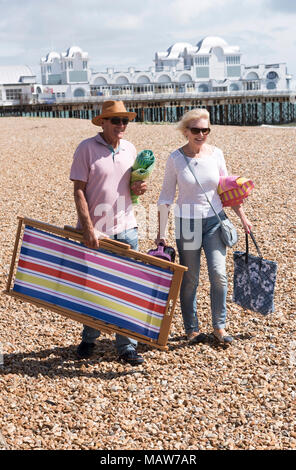 Elderly couple walking with a deckchair on a shingle beach. Southsea, England UK Stock Photo