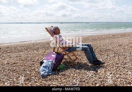 Elderly man wearing a knotted handkerchief on his head relaxing on the beach. Southsea, England UK Stock Photo