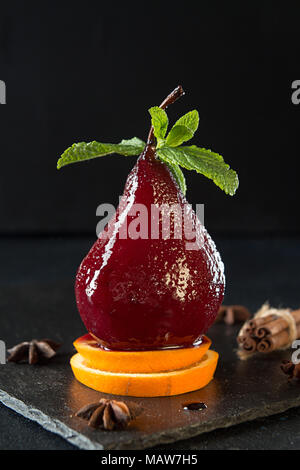 Pears in wine. Traditional dessert pears stewed in red wine on black background. Pears on orange fruit slices. Stock Photo