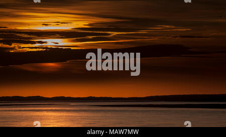 Dramatic sunset through clouds over the Menai Straits on the North Wales coast, as viewed from Caernarfon Stock Photo