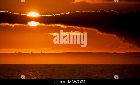 Dramatic sunset through clouds over the Menai Straits on the North Wales coast, as viewed from Caernarfon Stock Photo