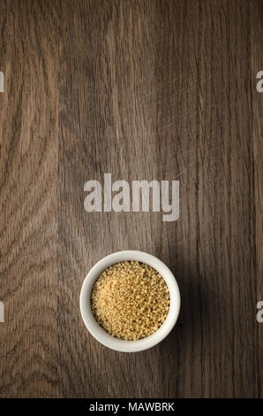 Overhead food background shot of small white bowl filled with couscous on old, scratched, dark oak wood surface. Copy space above. Stock Photo