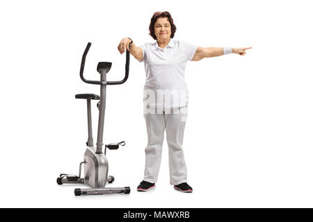 Full length portrait of an elderly woman leaning on an exercise bike and pointing isolated on white background Stock Photo