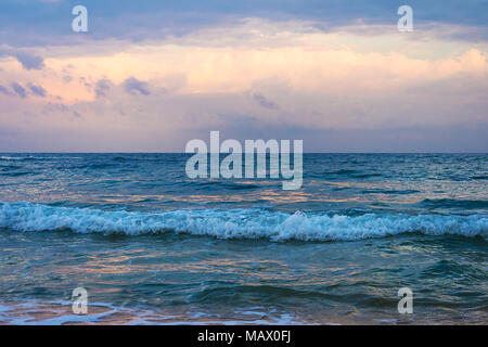 Background of colorful sky concept: Dramatic sunset with twilight color sky and clouds. Purple sky and blue water in the sea. Waves on water. Stock Photo