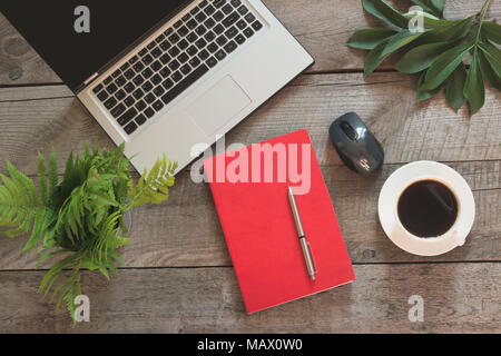 Open laptop with red notebook on office wooden desk table. Top view. Working process. Stock Photo