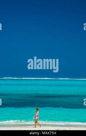 Woman walking along an idyllic tropical beach in Turks and Caicos Islands, Caribbean with golden sand and an azure blue ocean conceptual of travel and Stock Photo