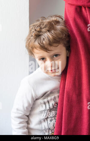 Child hiding behind a red curtain with smiling gesture Stock Photo