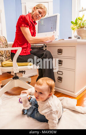 A woman working in her home office with her child close by. Stock Photo