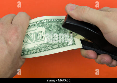 A bundle of paper bills is punctured by a stapler on an orange background Stock Photo