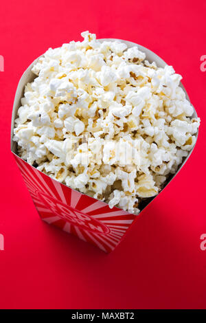 Striped box with popcorn on red background. Stock Photo