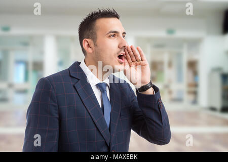 Young real estate agent or realtor shouting with hand on mouth as loudly calling or yelling on lobby background Stock Photo