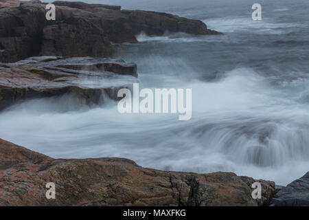 Waves crashing over the rocks at Schoodic Point, part of Acadia National Park in Maine, USA, at sunset on a cloudy evening. Stock Photo