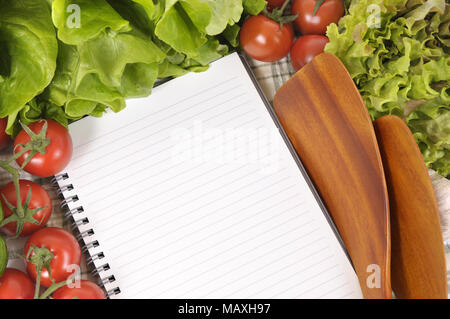 Selection of salad vegetables with blank recipe book or shopping list and wooden serving spoons. Stock Photo