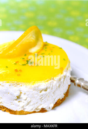 vertical image of lemon mousse cheesecake on a white plate with a colored green background Stock Photo