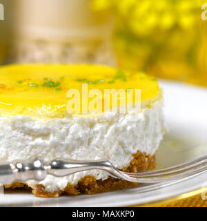 restaurant setting of a lemon mousse cheesecake a silver fork on a white plate soft background with  yellow flowers and to ad copy space Stock Photo