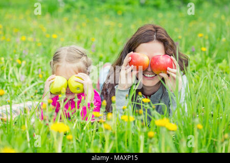 Mother and daughter lying on green meadow and holding apples Stock Photo