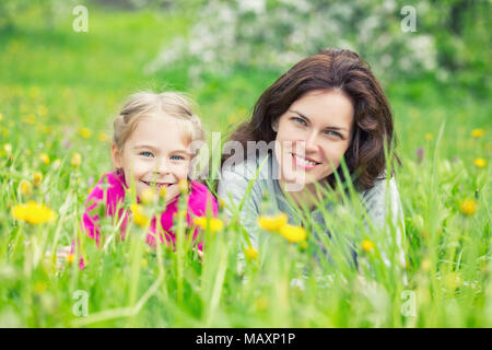 Mother and daughter lying on green summer grass with blooming yellow flowers Stock Photo