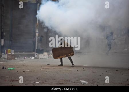 April 5, 2018 - Srinagar, J&K, India - A tear gas shell fired by Indian policeman explodes near a Kashmiri student protester during clashes in Srinagar, Indian administered Kashmir. Fierce clashes broke out between government forces and students in Srinagar on Thursday as the valley continued to remain tense over the killing of 17 people including 13 militants and 4 civilians in separate encounters in south Kashmir. Police used tear smoke shells to chase away the protesters. The violence rocked Kashmir valley on the day when authorities lifted restrictions after four days of the shutdown. (Cre Stock Photo