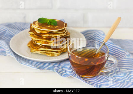 fresh baked pancakes with mint in white plate and cup of tea on blue linen on white background Stock Photo