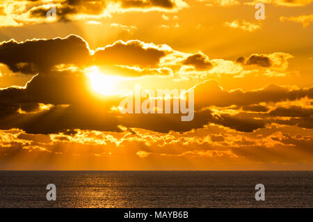 Dramatic sunset over water with rays of sun showing through and lighting up the sea. Stock Photo