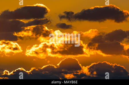 Dramatic clouds in the sky with orange colours from the sun lighting up the clouds as the sun sets. Stock Photo