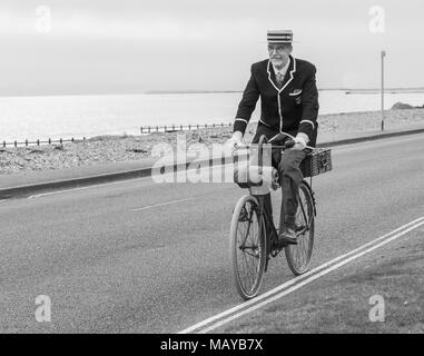 Senior man riding a Victorian bicycle dressed in period clothing and straw boater hat, in the UK, in black and white. Old cyclist riding vintage bike. Stock Photo
