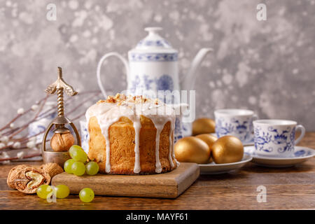 Easter cake and golden eggs with a teapot and teacups. Delicious homemade Easter cake with nuts and raisins on a table decorated for Easter. Beautiful Stock Photo