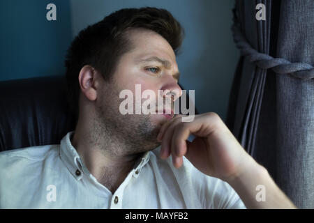 Caucasian man sitting in black sofa in sad mood. He is thinking about future plans or problems Stock Photo
