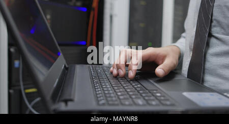 IT data specialist working on laptop on maintaining server rack Stock Photo