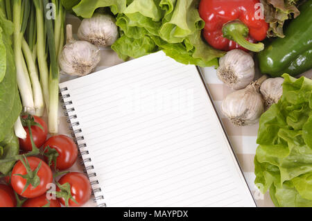 Selection of salad vegetables with lined notebook on a check tablecloth. Stock Photo