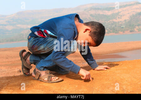 Little boy writing on ground with his finger at Tamihini ghat at Pune Stock Photo
