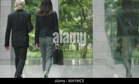 corporate businessman and businesswoman walking out of modern office building. Stock Photo
