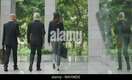 multinational corporate businessmen and businesswoman leaving walking out of modern office building. Stock Photo