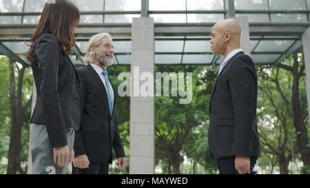 three corporate business people standing and talking in lobby of modern office building. Stock Photo