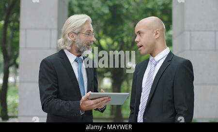 caucasian and latino corporate executives discussing business using digital tablet. Stock Photo